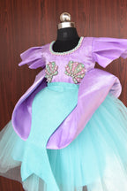 Close-up of a turquoise and purple dress with embellishments on a wooden surface